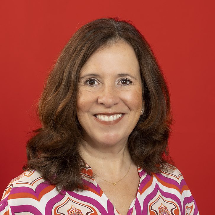 Inhaberin-Standpunkt-finden Foto-zeigt-Porträt-einer-Frau-mit-schulterlangem-braunem-Haar-vor-rotem-Hintergrund-mit-freundlichem-offenem-Blick-in-die-Kamera